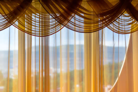 Translucent curtains of cream shades. Outside the window is a landscape.