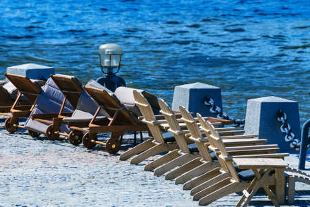 Wooden sunbeds stand on the stone bank of the river near the waterの写真素材