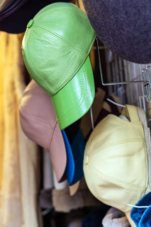 Multi-colored baseball caps made of artificial leather hang on a metal hangerの写真素材