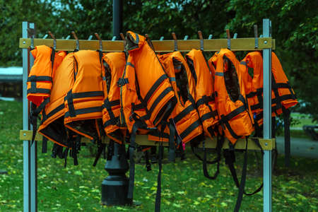 Many orange life jackets hang on a hanger in a row