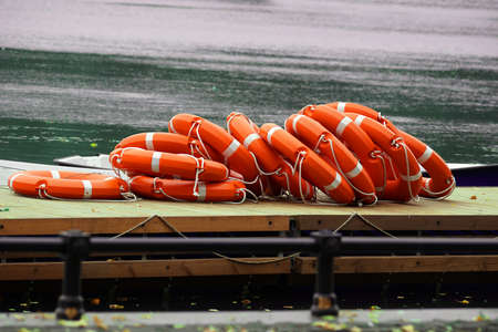 Many plastic lifebuoys lie on a wooden pier near the boats.