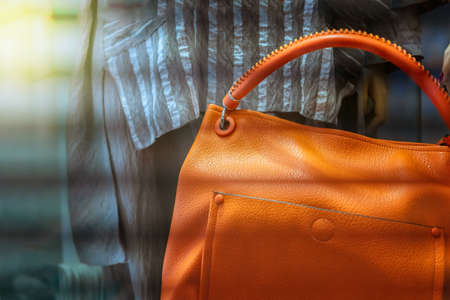 Women's bag made of leather bright orange color against the background of striped clothes. Behind the glass.の写真素材