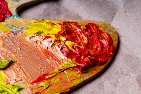 Red and yellow oil paints are mixed on a wooden palette.の写真素材