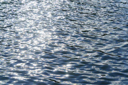 Dark water with shallow waves and a light line from the sun. Glare on the water.
