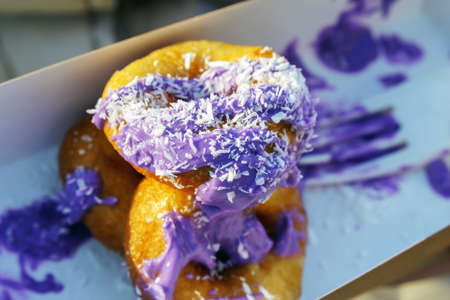 Fast food. Small donuts with purple glaze are sprinkled with coconut crumbs. In a cardboard box.の写真素材