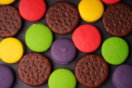 Colorful macarounds and round chocolate chip cookies are laid out on a dark background. Bright colors.の写真素材