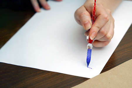 Calligraphy training. A woman's hand holds a glass feather with blue ink and begins to write on a...