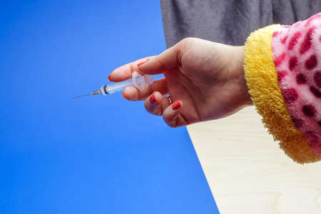 A woman's hand in a halaya with a red manicure holds a syringe.の写真素材