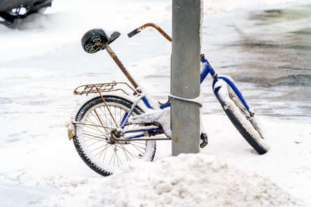 The bike is strapped to a concrete pole and covered with snowの写真素材