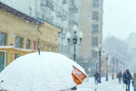 The large orange umbrella is covered with a thick layer of snow. In the distance are silhouettes of people. Its snowingの写真素材
