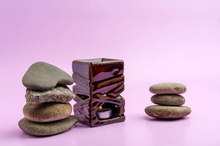 Aromatic lamp with a burning candle of square shape next to a pyramid of stones on a pink background.の写真素材