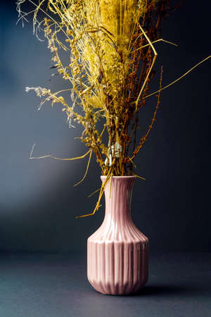 Dry yellow plants in a light pink vase on a dark background.の写真素材