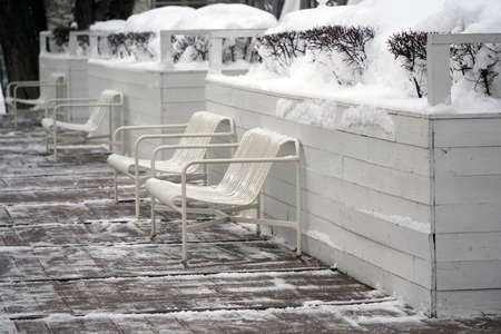Metal benches on the snow-covered terrace with wooden deckingの写真素材