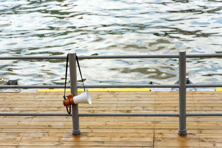 Handheld portable megaphone loudspeaker hanging on the railing of the river pier.