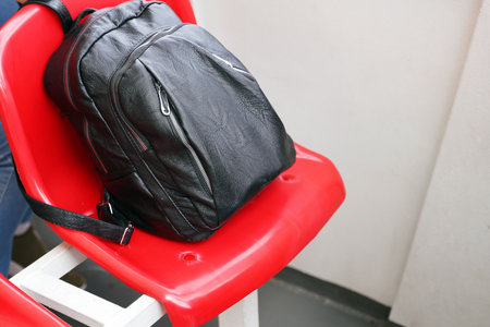A black backpack made of artificial leather lies on a red plastic seat.の写真素材