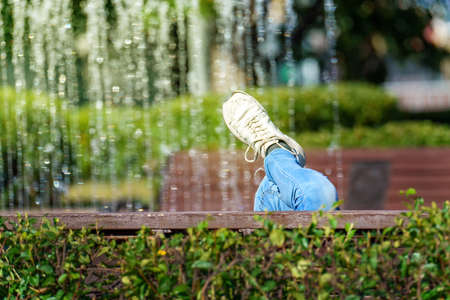 A foot in an old sneaker against the background of the fountain. A person rests in the park.の写真素材