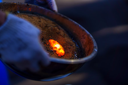 Bright glowing piece of molten metal in a bowl of sand held by a manの写真素材