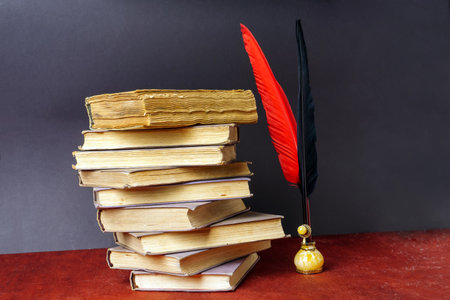 Pens for writing red and black are in the inkwell next to a stack of old booksの写真素材