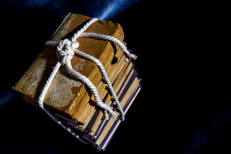 A stack of old books are tied with rope on a dark background.の写真素材