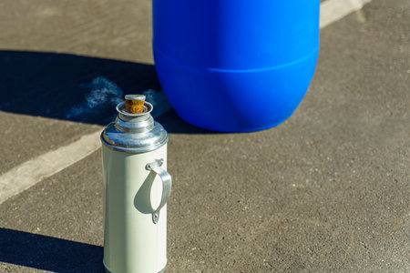 Vintage flask with cork cap from which comes white steam stands on the asphaltの写真素材