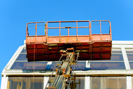 Metal basket for workers raised on the boom of the crane above the glass ceiling of the building