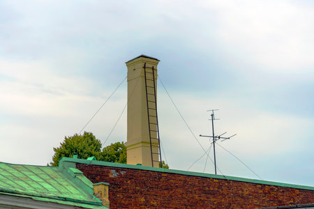 Brick chimney on the roof of the building with a leaning metal staircaseの写真素材