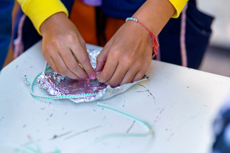 Hands of a child who wraps a synthetic thread in foil to make a toy in a thermal pressの写真素材