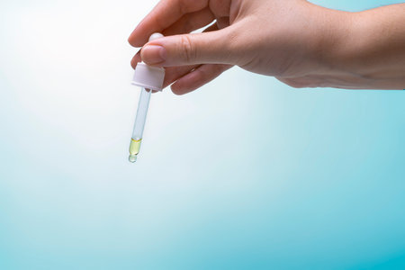 Eyedropper with yellow oil in the hand on a blue backgroundの写真素材