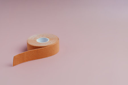 Flesh-coloured cosmetic adhesive tape rolled on a light pink backgroundの写真素材