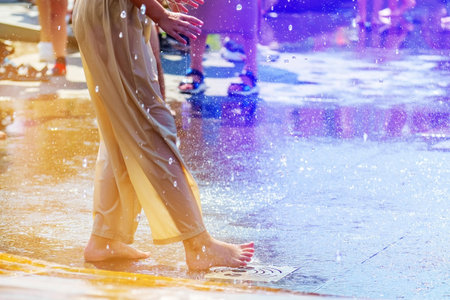 Feet of a man playing with jets of water in a fountain in the summerの写真素材