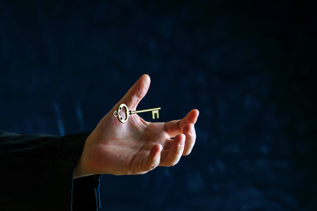 Above the palm of a man in black clothes, a vintage copper key levitatesの写真素材