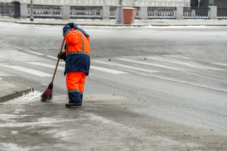 A janitor in overalls sweeps an asphalt road with a broomstickの写真素材
