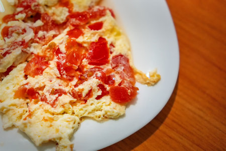 Egg omelette with milk and pieces of red tomatoes on a white plate