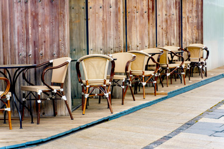 Elegant chairs and tables stand near the wall of a street restaurant in a row near the sidewalkの写真素材