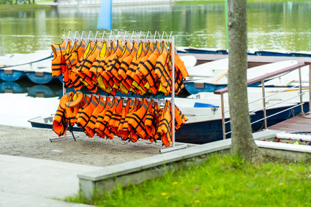 Orange life jackets hang on a metal rack at a boat station near the lakeの写真素材
