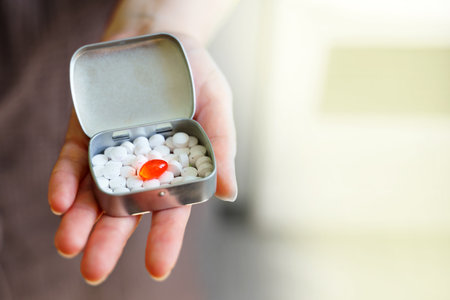 A womans hand holds a box of pills, one of which is redの写真素材