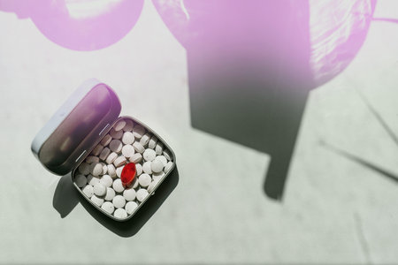 Metal box with round white tablets and one red in the bright sunの写真素材