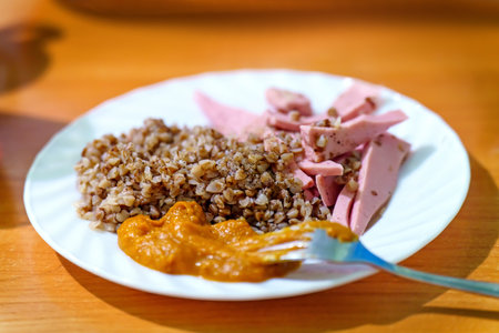 Buckwheat porridge with fried boiled sausage and zucchini caviar on a plateの写真素材