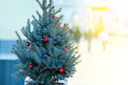 Small Christmas tree with red balls on the sidewalk, silhouettes of peopleの写真素材