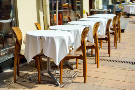 Row of square tables with white tablecloths at an outdoor restaurantの写真素材