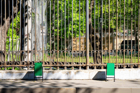 Two green trash bins on the sidewalk by a metal fenceの写真素材