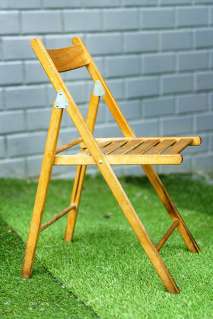 Foldable wooden chair on synthetic grass near a wall, blending indoor comfort with outdoor vibes