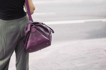 girl carries a large leather sports bag on her shoulder by the roadside, ready for actionの写真素材