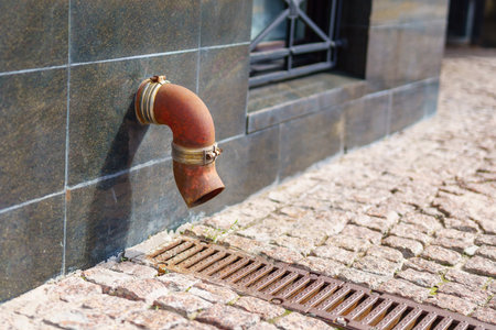 curved rusty downspout embedded in the wall of a modern house for roof water drainage, blending functionality and industrial design seamlesslyの写真素材