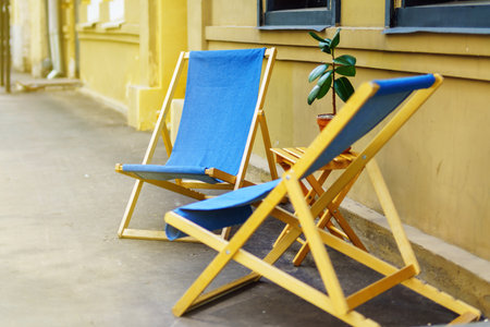 Folding wooden chairs with fabric seats placed on the sidewalk outside a store, offering outdoor...
