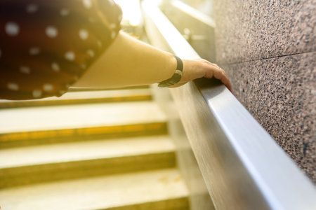 woman's hand reaches upward through metallic railings, striving to touch the sun. This image symbolizes hope, aspiration, and the pursuit of dreams against the constraints of modern lifeの写真素材
