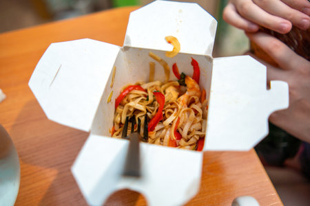 cardboard box cradles a vibrant stir-fried noodle dish, bursting with colorful vegetables and bright red peppers, embodying a fusion of flavors and culturesの写真素材