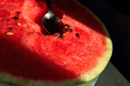 ripe red watermelon, its flesh exposed, invites indulgence with a spoon resting in its cavity, embodying summer's sweetness and the joy of shared momentsの写真素材