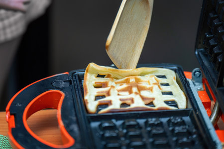 bamboo spatula gently lifts a perfectly golden waffle from an electric waffle maker, capturing the warmth and aroma of a homemade breakfast delightの写真素材