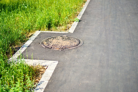 lateral curve of an asphalt sidewalk designed to accommodate a manhole cover, illustrating urban infrastructure's functional and aesthetic integration in cityscapesの写真素材